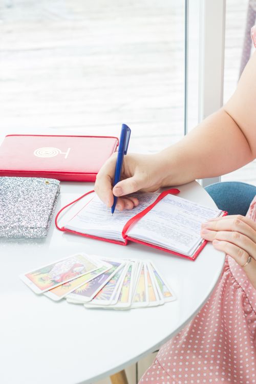 En person skriver i en journal bredvid tarotkort i dagsljus